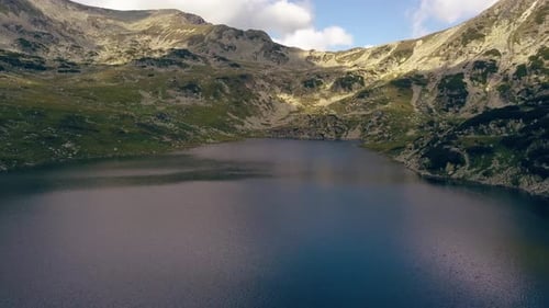 Wide stationary aerial drone flying over a lake looking towards a mountain range.