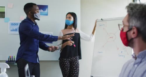 Diverse male and female office colleagues wearing face masks giving presentation at modern office