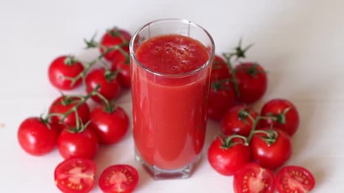Glas mit Tomatensaft auf weißem Hintergrund, ein Tropfen Saft fällt ins Glas