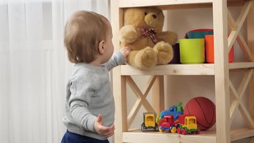 ребенок тянется к игрушке на полке