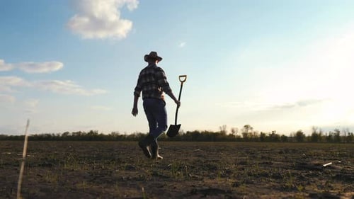 Adult Man Walking with Shovel in Rural Field