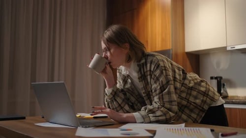 Schöne junge Frau arbeitet am Laptop, während sie im Wohnzimmer sitzt und Kaffee trinkt
