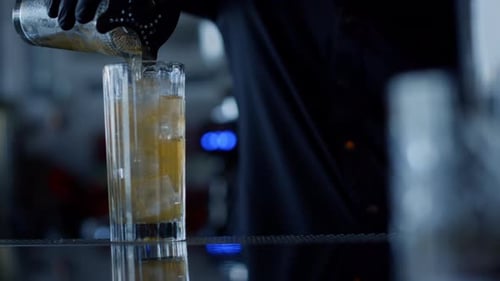 Bartender pours cocktail into glass over ice