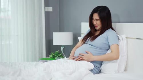 schwangere Frau hat Bauchschmerzen auf einem Bett