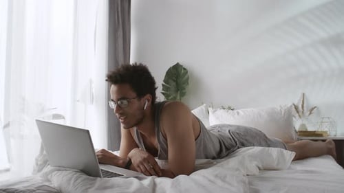 Man Uses Laptop While Lying on Bed