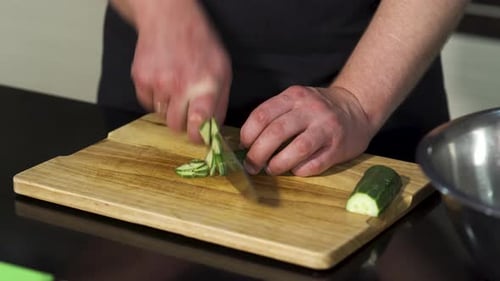 Person Slicing Cucumber on Cutting Board in Kitchen