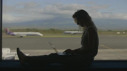 Woman Working on Laptop in Airport Terminal