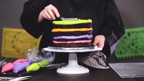 Step by step. Baker assembling a chocolate cake with bright colorful buttercream frosting for Dia de