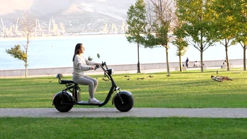 Jeune fille en scooter électrique est à cheval dans le parc public au matin ensoleillé