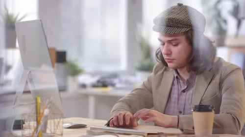 Mann in flacher Mütze und Jacke arbeitet im Büro am Computer