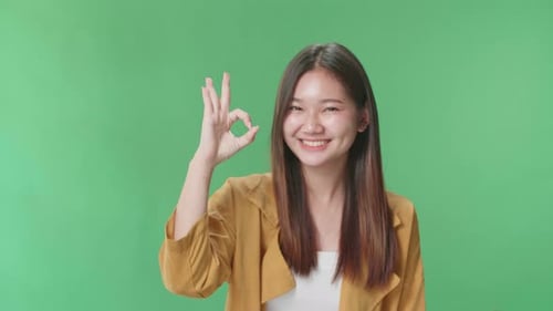 Ein Porträt einer glücklichen asiatischen Frau, die im Greenscreen-Studio vor der Kamera eine Okay-Geste zeigt