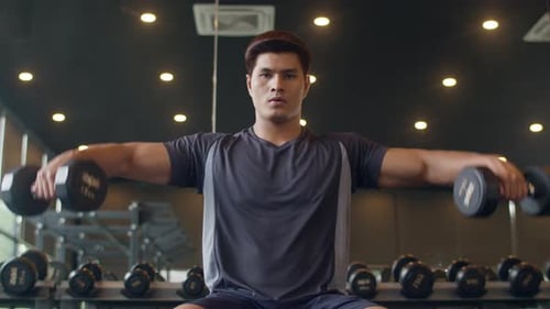 Young Adult Male Lifts Dumbbells in Gym