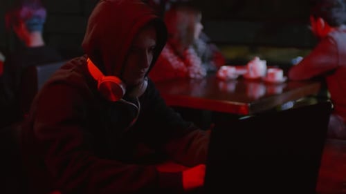 Hooded Hacker Sitting at Computer in Restaurant