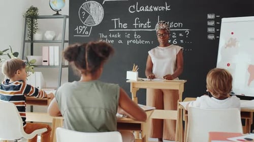 Afro-American Female Teacher Asking Question at Lesson in Primary School