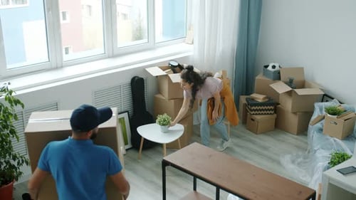 High Angle View of Young Male Worker Bringing Carton Boxes to New House and Talking to Woman