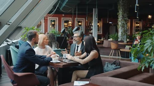 Cheerful Colleagues Mature and Young Men and Women Talking in Cafe During Lunch Break