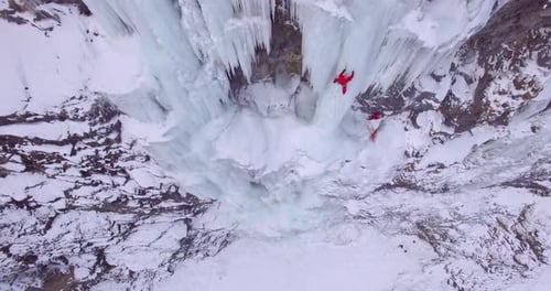 Aerial drone view of a man ice climbing on a frozen waterfall in the mountains