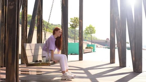 Jolie jeune femme calme se balançant sur une balançoire dans un parc municipal par une belle journée d'été ensoleillée.