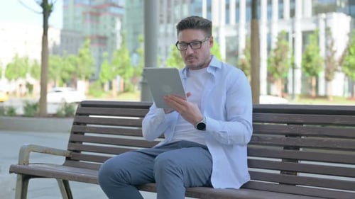 Man Sitting on Park Bench Using Tablet Device