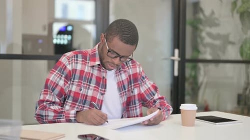 African Man Reading Reports While Sitting in Office