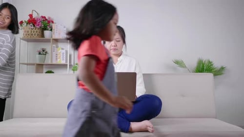La madre tranquila se sienta en el sofá trabajando en el portátil, los niños pequeños juegan, la madre tranquila se relaja en el sofá