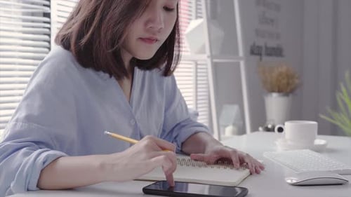 Woman Using Phone and Writing at Desk