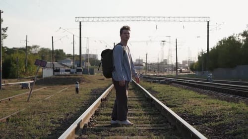 A Young Man with a Hiking Backpack Hitchhikes Walking on the Railroad on Foot
