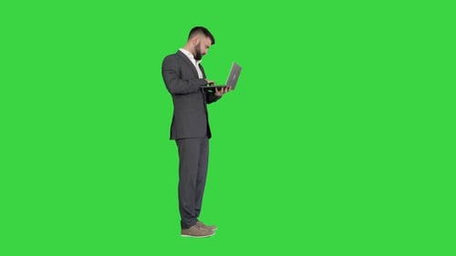 Handsome Businessman Standing and Working on Laptop on a Green Screen, Chroma Key.