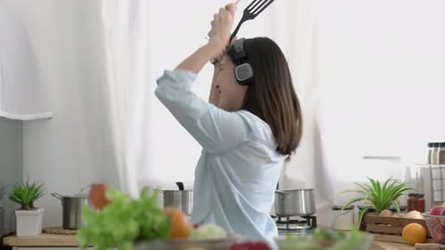 Young Woman Dancing in Kitchen with Cooking Utensils