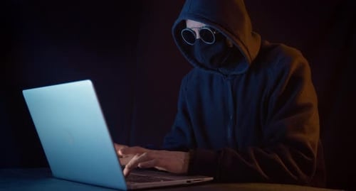 Hooded Figure Types on Laptop in Dark Room