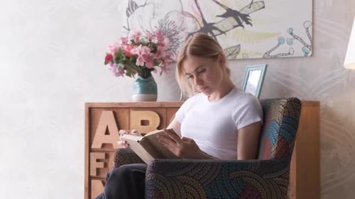 Happy woman reading a book while relaxing on Chair at home. A Young Blonde Woman
