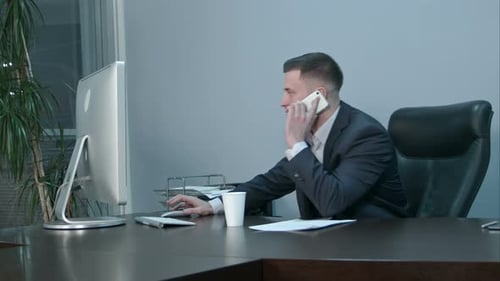 Young Caucasian Businessman Calling with Smartphone and Talking Seriously in Office