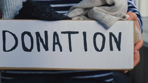 Female Volunteer Holding Donation Box with Old Used Toys and Clothes Indoors