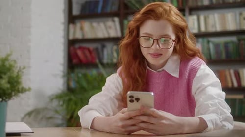 Attractive Student Woman Holding Modern Smartphone Texting Message in Home Office or Library