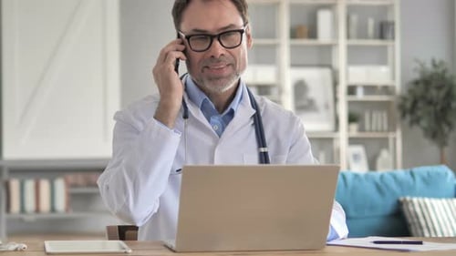 Adult Doctor Talking on Phone and Using Laptop