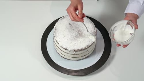 Top View of a Baker Pouring Melted White Chocolate on the Edges of the Cake so It Drips Down the
