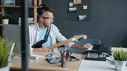 Talented Guy Playing Musical Instruments Keyboard and Guitar Recording Music Indoors in Studio