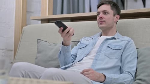 Young Adult Uses Remote Control on Couch at Home