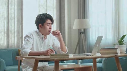 Asian Man Student Being Sleepy While Using Computer To Study Online At Home
