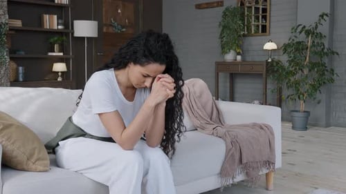Excité, frustrée, stressée, jeune femme assise dans la chambre sur le canapé, pensait tristement apprendre de mauvaises nouvelles