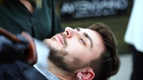 Junge schöne kaukasische Friseurin schneidet den Bart gutaussehender Mann im Modern Barbershop