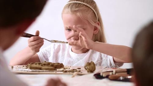 Child Carefully Shapes Clay at a Table
