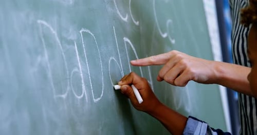 Child Learns to Write on Chalkboard with Assistance
