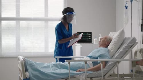 A Black Female Surgeon is Talking to an Elderly Male Patient Lying on a Hospital Bed