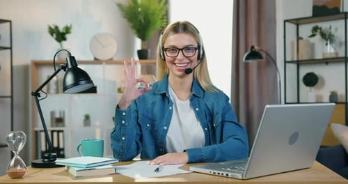 Rubia-Freelancer con auriculares inalámbricos que se colocan frente a la cámara y muestran el símbolo Ok