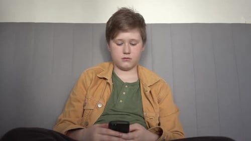Boy Using Smartphone Smiling on Couch Indoors