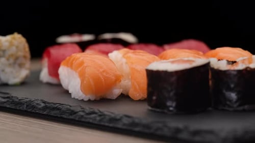 Sushi assortment rotating on a plate on black background. Nigiri salmon, tuna, hosomaki, uramaki. Ty