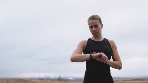 Athletic Woman in Sportswear Puts Timer on Her Smart Watch and Starts Jogging Outdoors Front View