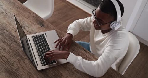 Young Adult Typing on Laptop with Headphones Indoors