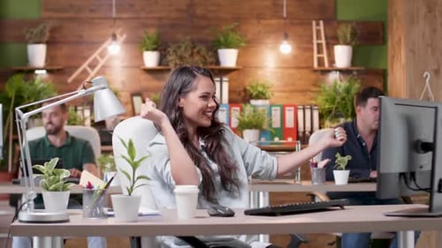Une femme gestionnaire danse joyeusement à son bureau pendant que ses collègues travaillent en arrière-plan